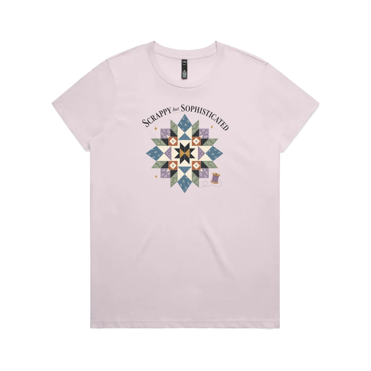 A pale mauve short-sleeve crewneck tshirt with the words 'Scrappy but Sophisticated' above a large star quilt block with a purple thread spool on the bottom right.