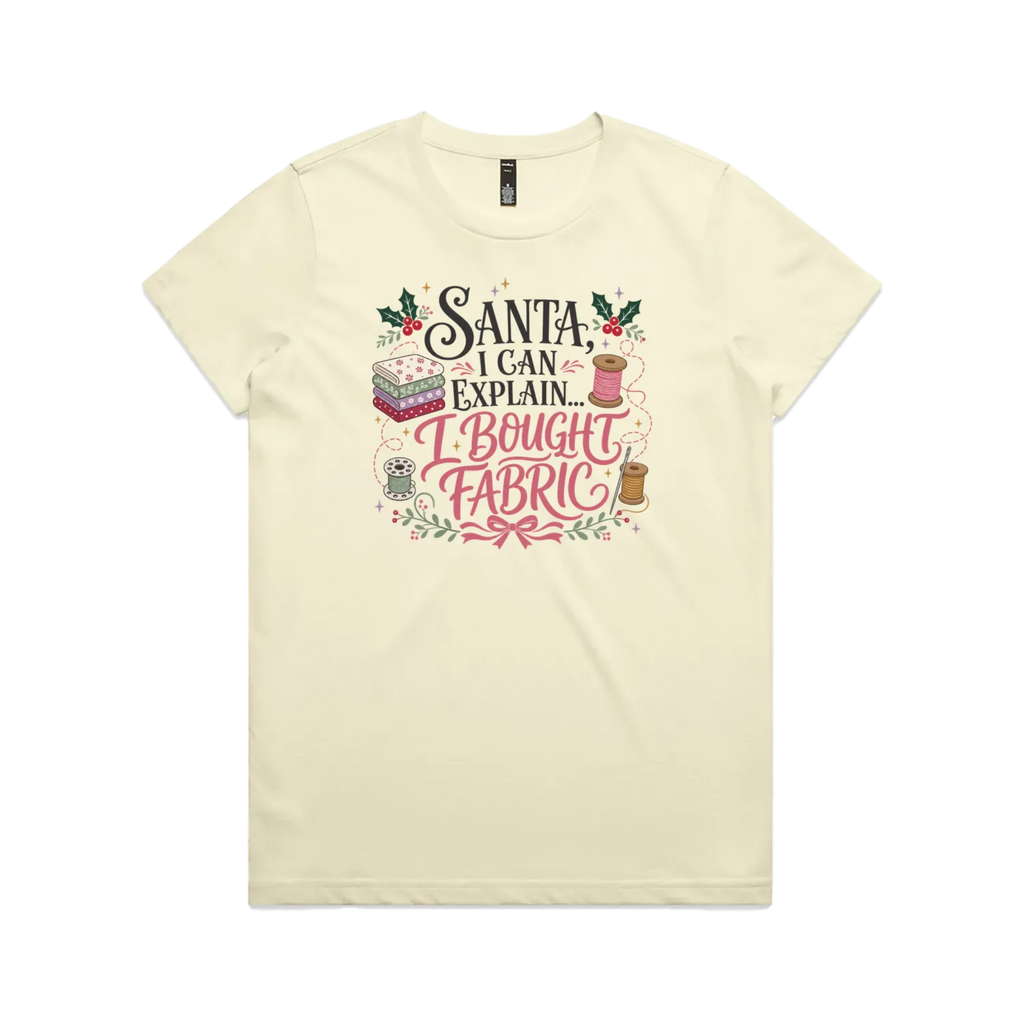 A pale butter yellow short-sleeve crewneck t-shirt with a festive Christmas-themed graphic on the chest. The graphic features the text 'Santa, I Can Explain...I Bought Fabric'.