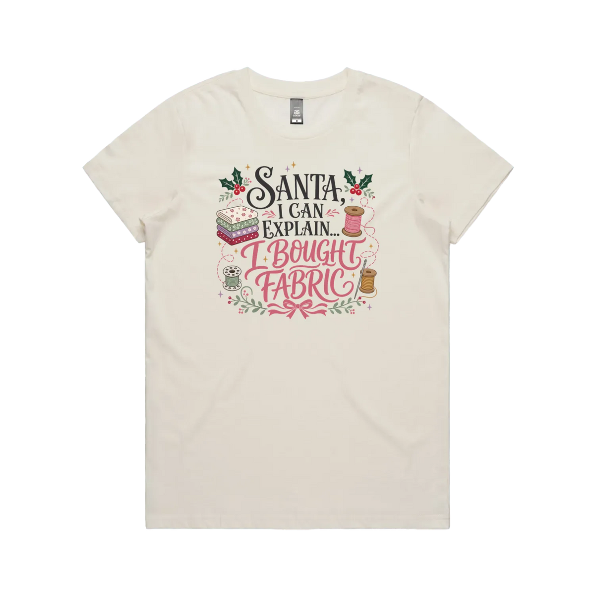 A pale cream short-sleeve crewneck t-shirt with a festive Christmas-themed graphic on the chest. The graphic features the text 'Santa, I Can Explain...I Bought Fabric'.