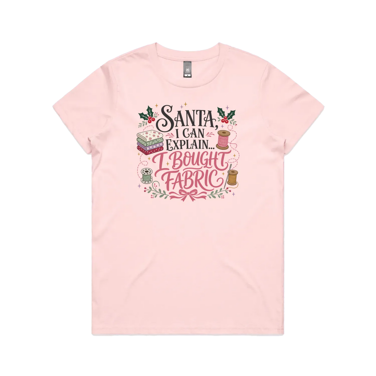 A pale pink short-sleeve crewneck t-shirt with a festive Christmas-themed graphic on the chest. The graphic features the text 'Santa, I Can Explain...I Bought Fabric'.
