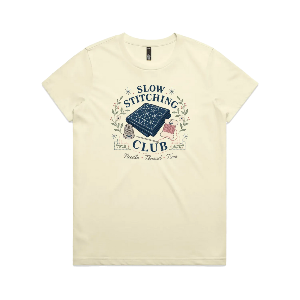 A pale butter yellow short-sleeved crewneck t-shirt with the graphic 'Slow Stitching Club' surrounding an illustration of a piece of sashiko stitched fabric, thimble, need and thread with small flowers and leaves.