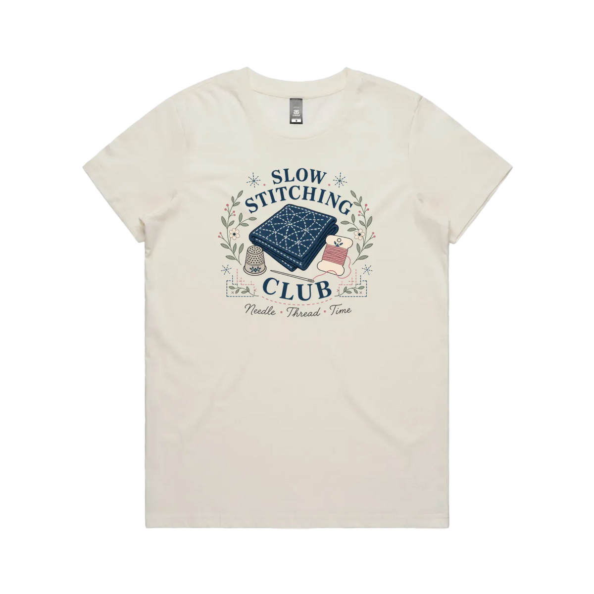 An off-white short-sleeved crewneck t-shirt with the graphic 'Slow Stitching Club' surrounding an illustration of a piece of sashiko stitched fabric, thimble, need and thread with small flowers and leaves.