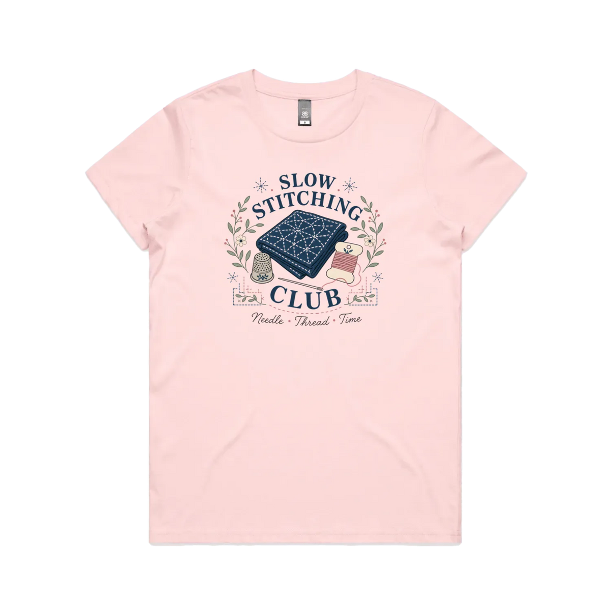 A pale pink short-sleeved crewneck t-shirt with the graphic 'Slow Stitching Club' surrounding an illustration of a piece of sashiko stitched fabric, thimble, need and thread with small flowers and leaves.