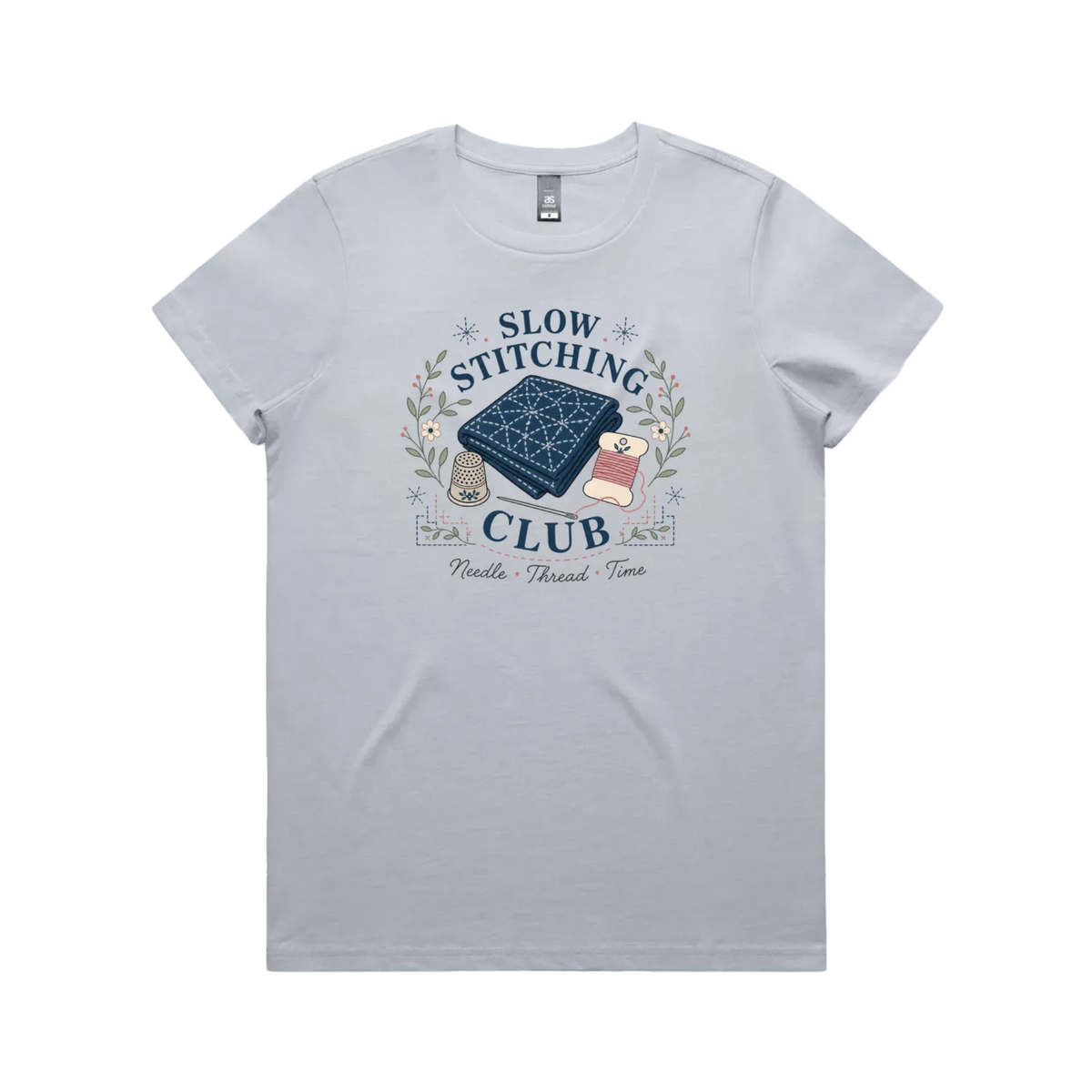 A powder blue short-sleeved crewneck t-shirt with the graphic 'Slow Stitching Club' surrounding an illustration of a piece of sashiko stitched fabric, thimble, need and thread with small flowers and leaves.