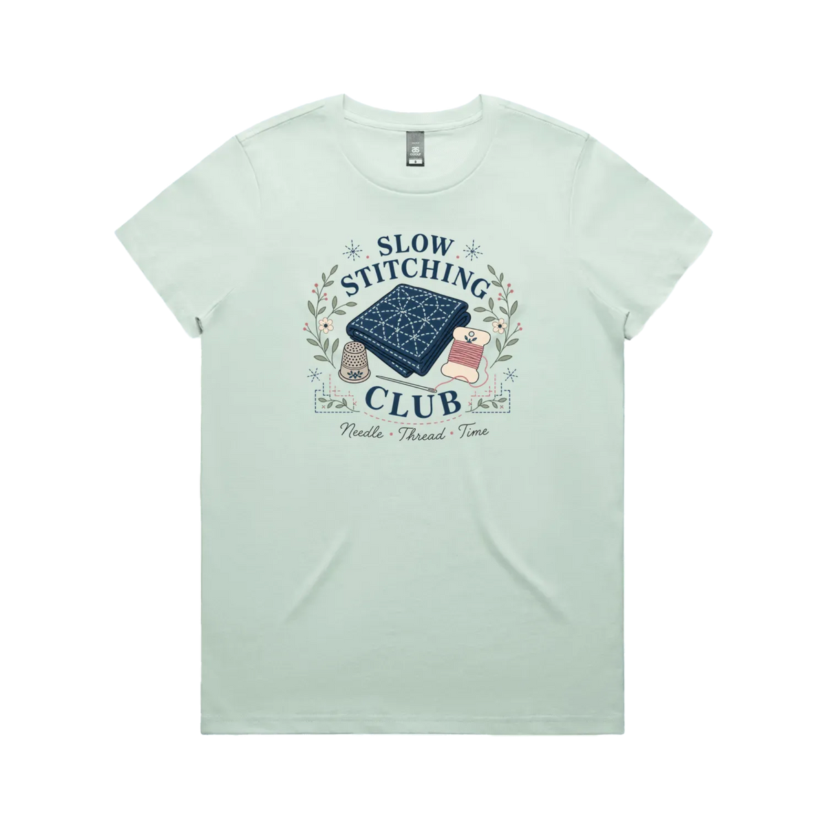 A pale mint green short-sleeved crewneck t-shirt with the graphic 'Slow Stitching Club' surrounding an illustration of a piece of sashiko stitched fabric, thimble, need and thread with small flowers and leaves.