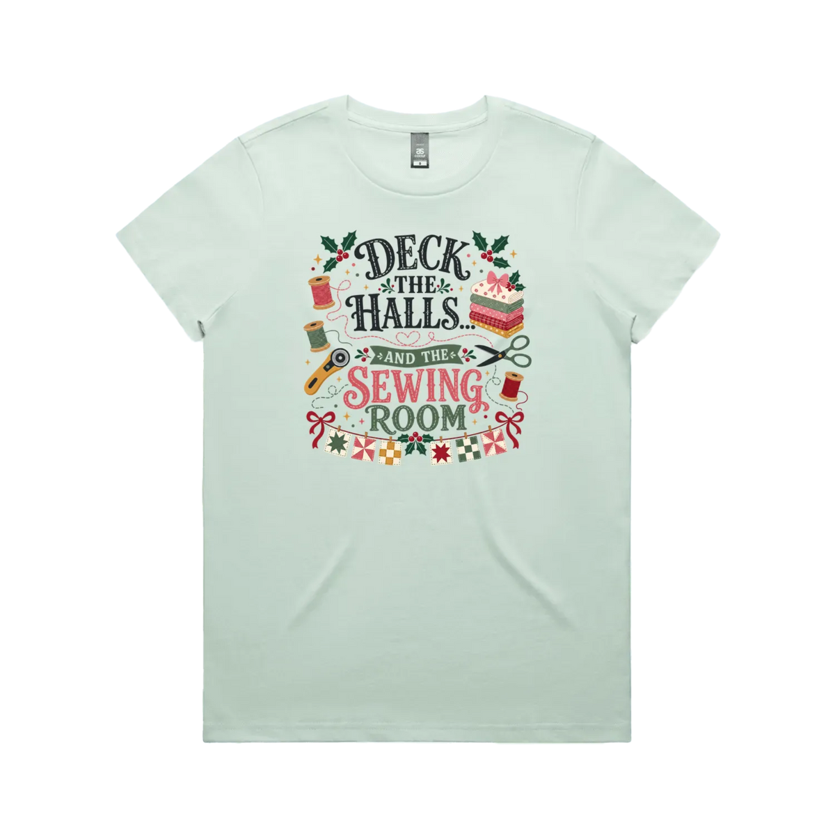 A pale seafoam green short-sleeve crewneck t-shirt featuring a colorful graphic print on the front with sewing-themed illustrations and the text 'Deck the Halls and the Sewing Room'.