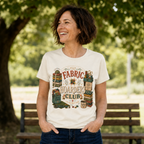 A dark haired woman standing in front of a park bench wearing a graphic t-shirt with the words 'The Fabric Hoarders Club' surrounded by illustrations of fabric bundles and quilting tools.
