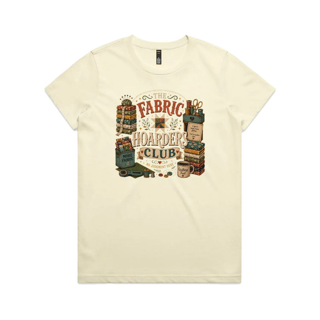 A pale butter yellow short-sleeve crewneck t-shirt with a vintage style graphic featuring the words 'The Fabric Hoarders Club' surrounded by fabric stacks, a coffee mug and quilting tools.