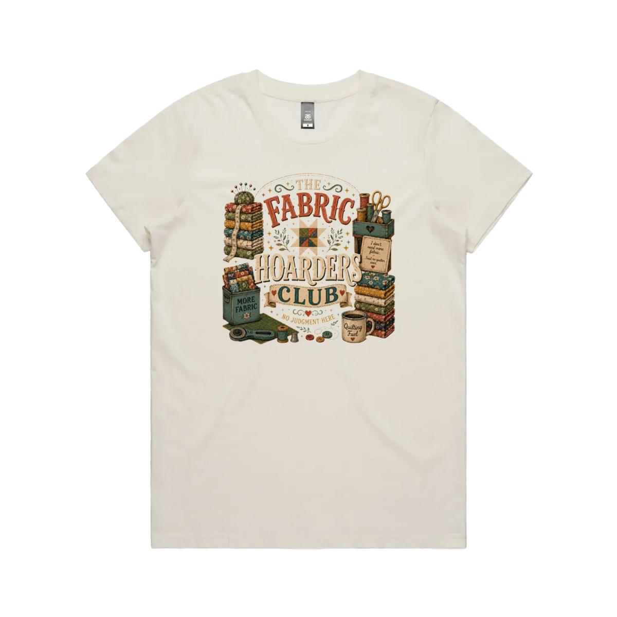 A pale cream short-sleeve crewneck t-shirt with a vintage style graphic featuring the words 'The Fabric Hoarders Club' surrounded by fabric stacks, a coffee mug and quilting tools.