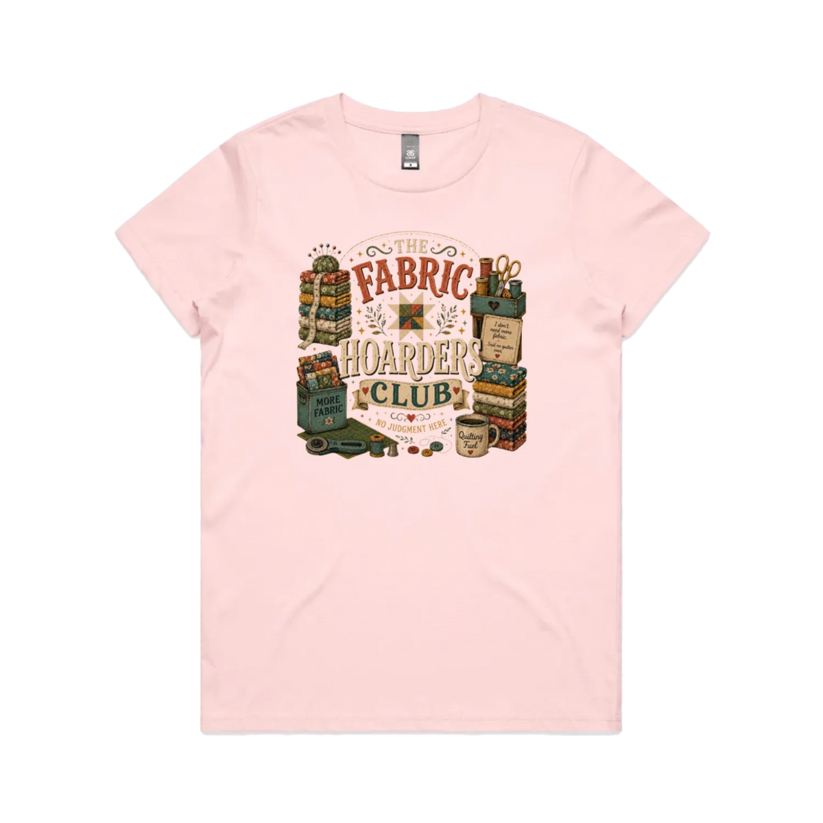 A pale pink short-sleeve crewneck t-shirt with a vintage style graphic featuring the words 'The Fabric Hoarders Club' surrounded by fabric stacks, a coffee mug and quilting tools.