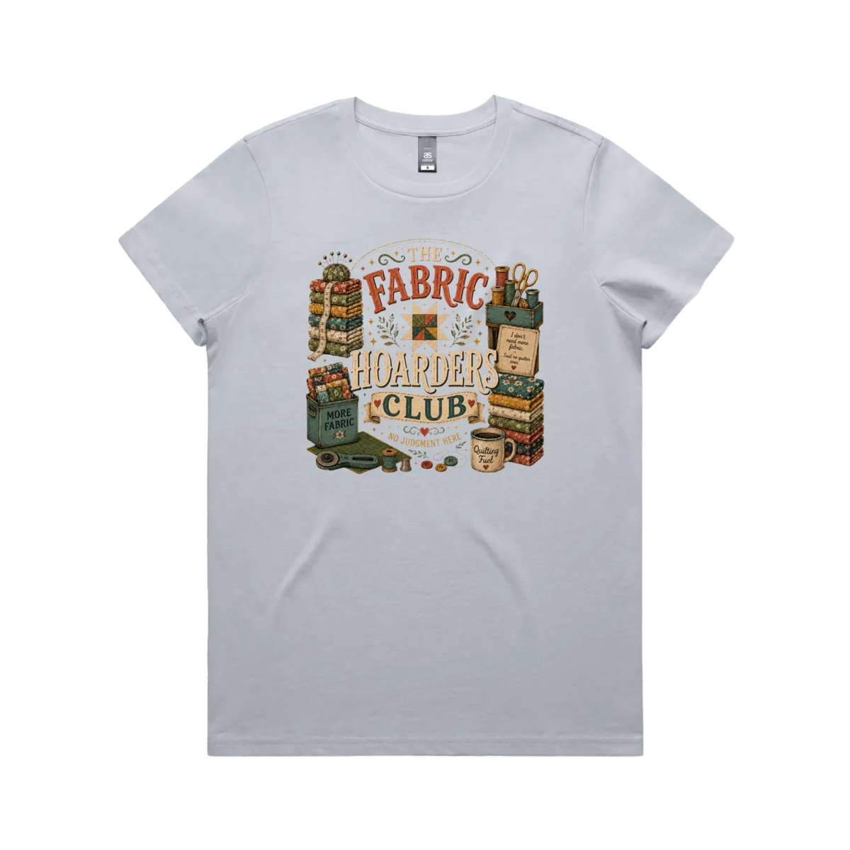 A powder blue short-sleeve crewneck t-shirt with a vintage style graphic featuring the words 'The Fabric Hoarders Club' surrounded by fabric stacks, a coffee mug and quilting tools.