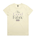 A very pale yellow short-sleeve crewneck t-shirt featuring a graphic print on the front that reads 'The Good Fabric' in dark gray and lavender lettering, with a small fabric bundle illustration below.