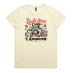 A pale butter yellow short-sleeve t-shirt with a colorful retro graphic on the chest featuring a vintage rotary phone made of fabric pieces, a spool of thread, shopping bags, and the text 'The Quilt Shop Called, I Answered'.