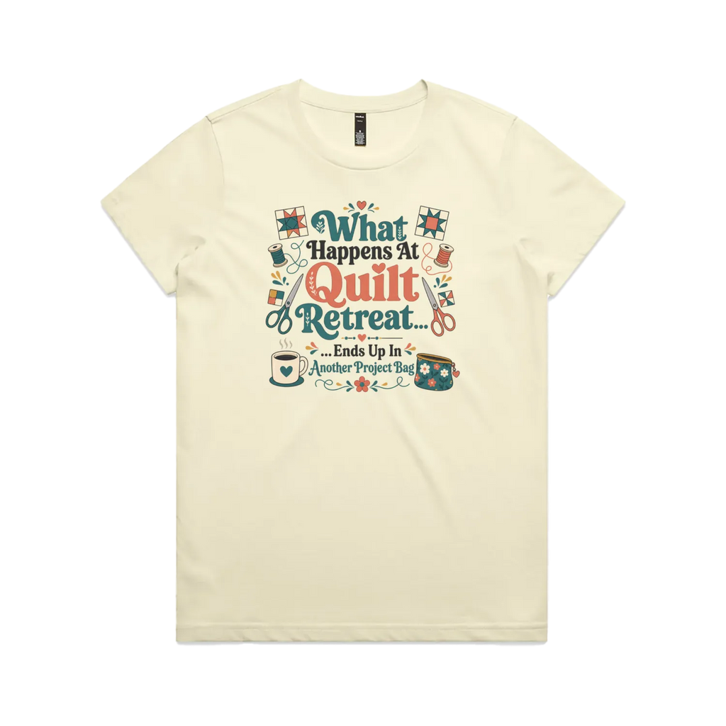 A pale butter yellow short-sleeve graphic t-shirt with the words 'What Happens at Quilt Retreat...ends up in another project bag'. The words are surrounded by quilt blocks thread spools, scissors, a coffee mug and zippered bag.
