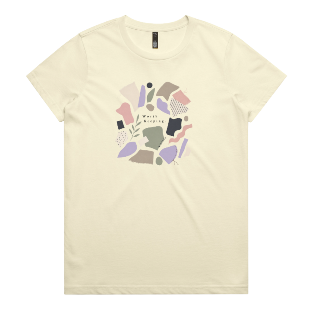 A pale yellow crewneck t-shirt featuring a central graphic of abstract pastel shapes in pink, purple, beige, and brown, with the text 'Worth Keeping' written in the center.