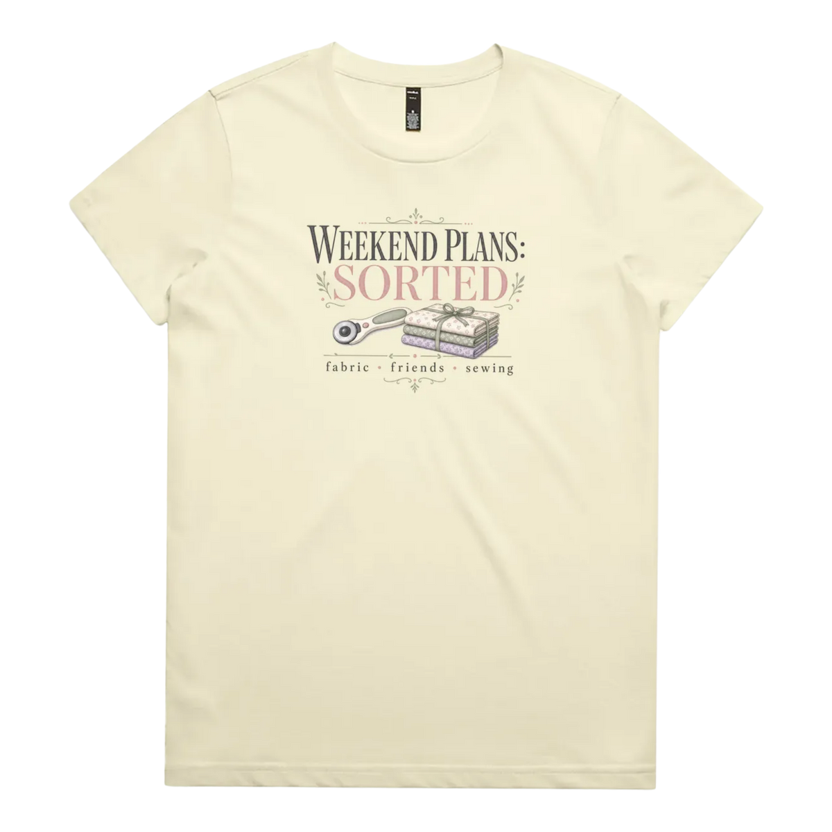 A pale butter yellow short-sleeve t-shirt with a vintage-style graphic on the chest reading 'WEEKEND PLANS: SORTED' above an illustration of a rotary cutter and tied fabric bundle, with 'fabric + friends + sewing' below.