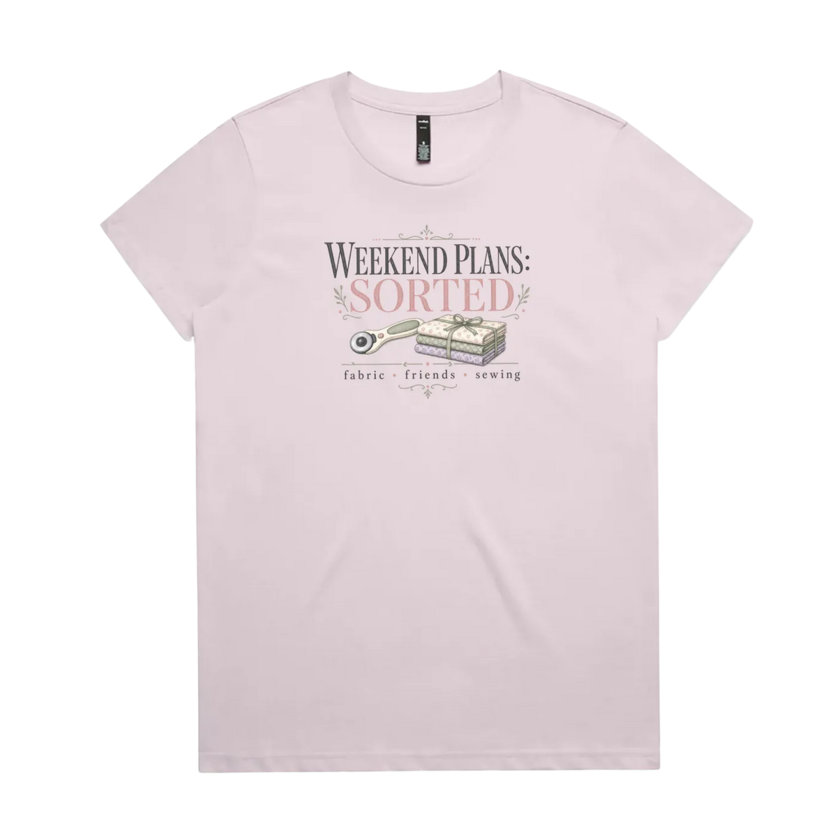 A light mauve short-sleeve t-shirt with a vintage-style graphic on the chest reading 'WEEKEND PLANS: SORTED' above an illustration of a rotary cutter and tied fabric bundle, with 'fabric + friends + sewing' below.