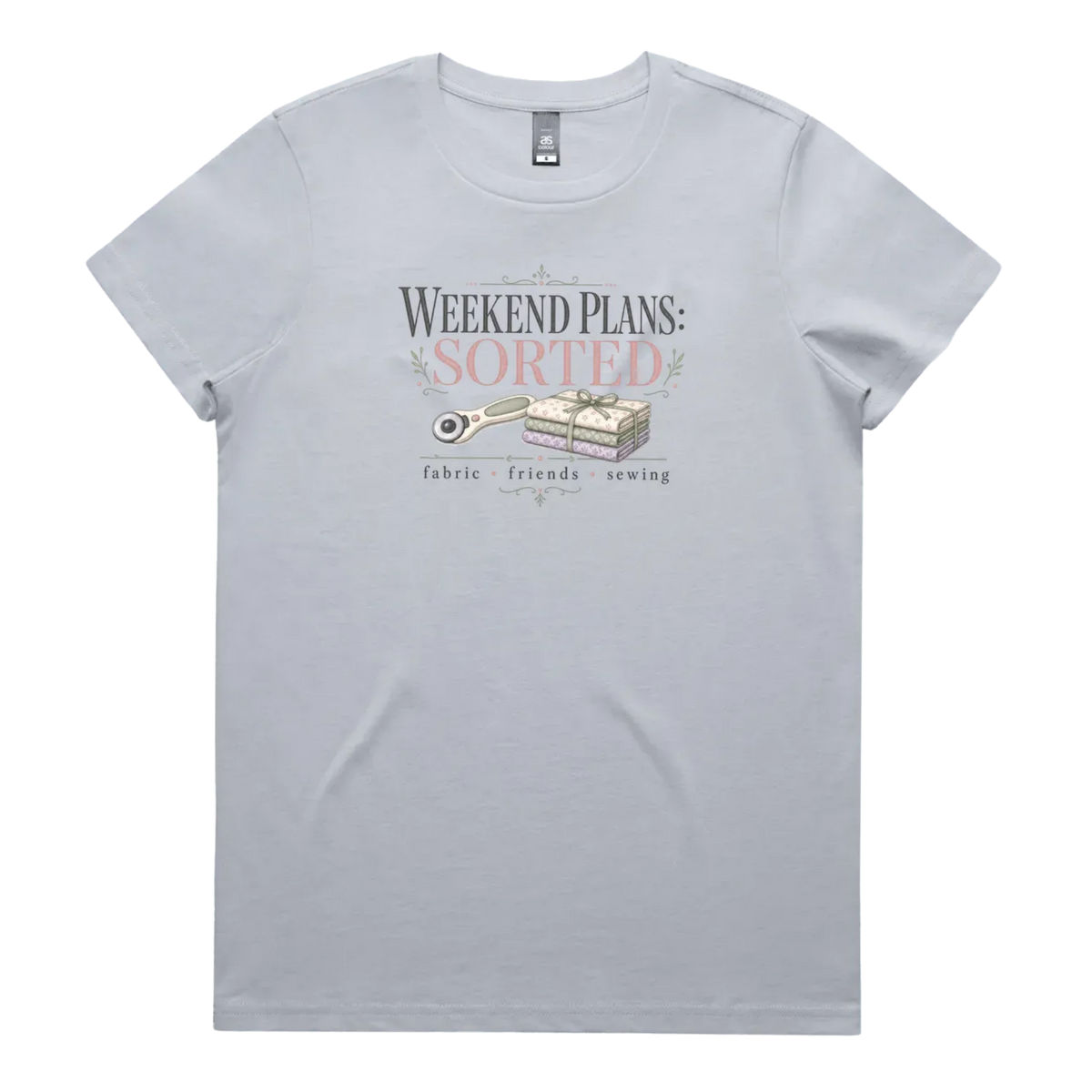 A powder blue short-sleeve t-shirt with a vintage-style graphic on the chest reading 'WEEKEND PLANS: SORTED' above an illustration of a rotary cutter and tied fabric bundle, with 'fabric + friends + sewing' below.