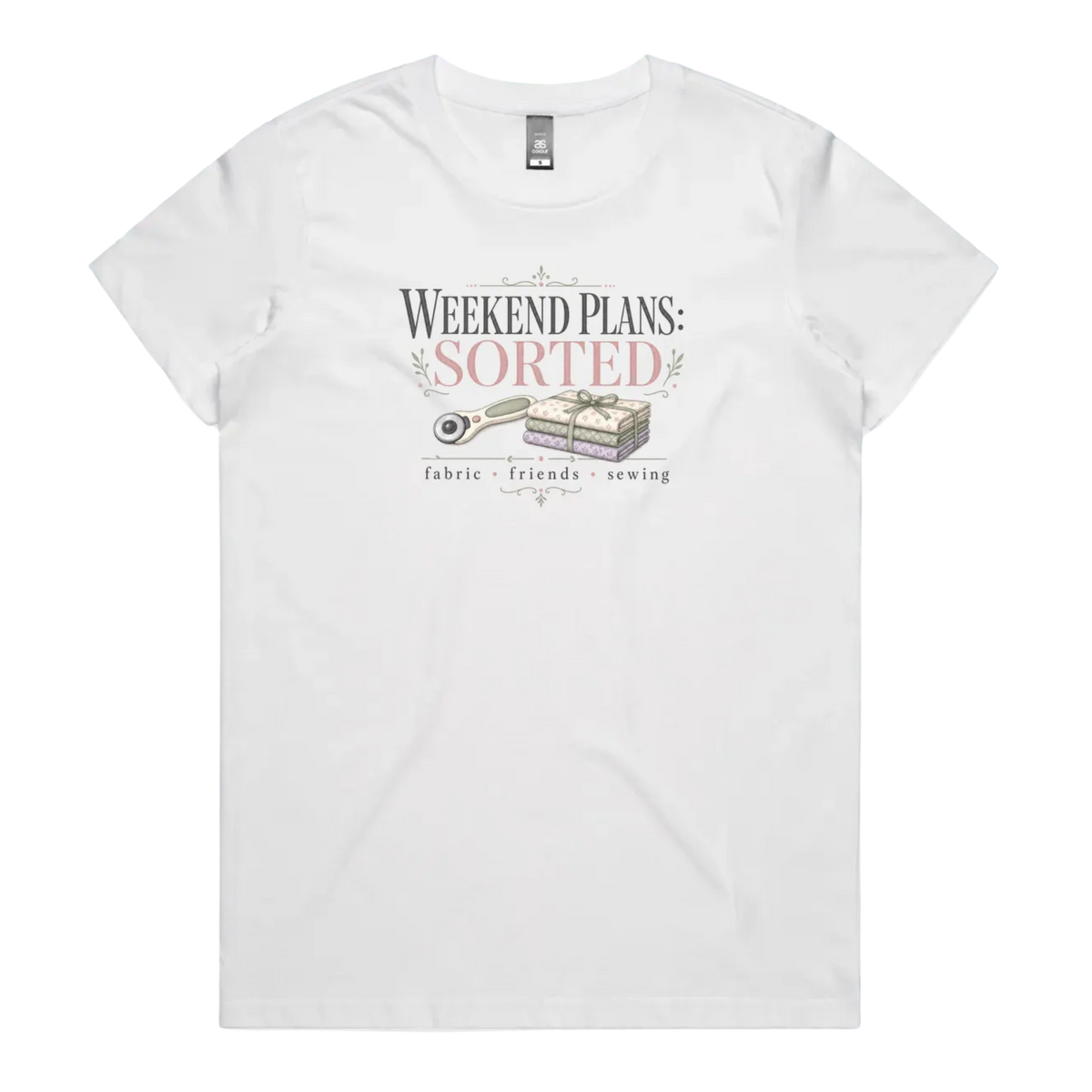 A white short-sleeve t-shirt with a vintage-style graphic on the chest reading 'WEEKEND PLANS: SORTED' above an illustration of a rotary cutter and tied fabric bundle, with 'fabric + friends + sewing' below.